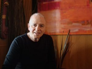 Peter Riese mit dunklem Sweat-Shirt vor hellem Hintergrund mit Bild
